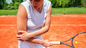 一名女子在网球场上痛苦地抱着自己的胳膊肘。