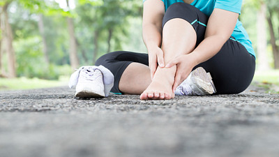 女人坐在人行道上与她的鞋和袜子握着她的脚踝疼痛。