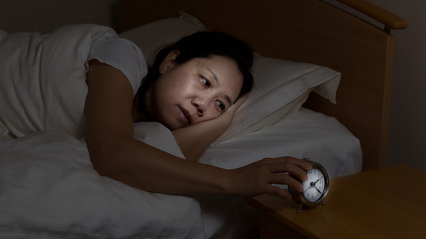Woman awake in bed staring at an alarm clock