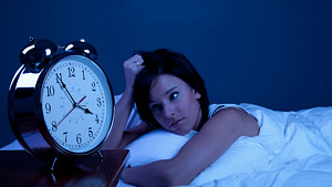 Woman laying in a dark room with a clock reading 3:55