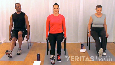 Three people sitting in chairs doing the seated hamstring stretch
