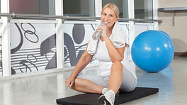 一名女子在锻炼后休息，喝着一瓶水，背景是一个健身球